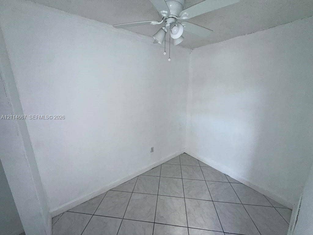Neutral interior space featuring white walls, diagonal-set ceramic floor tiles, and a white ceiling fan with integrated lighting