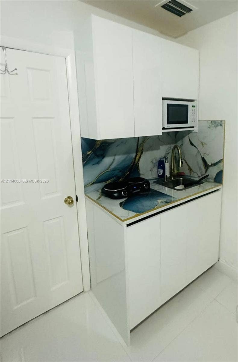 35 SW 28th Road, #B, Miami, Miami, FL 33129 Compact kitchenette featuring white flat-panel cabinetry, patterned stone-style backsplash, integrated microwave, drop-in sink with a high-arch faucet, and polished flooring