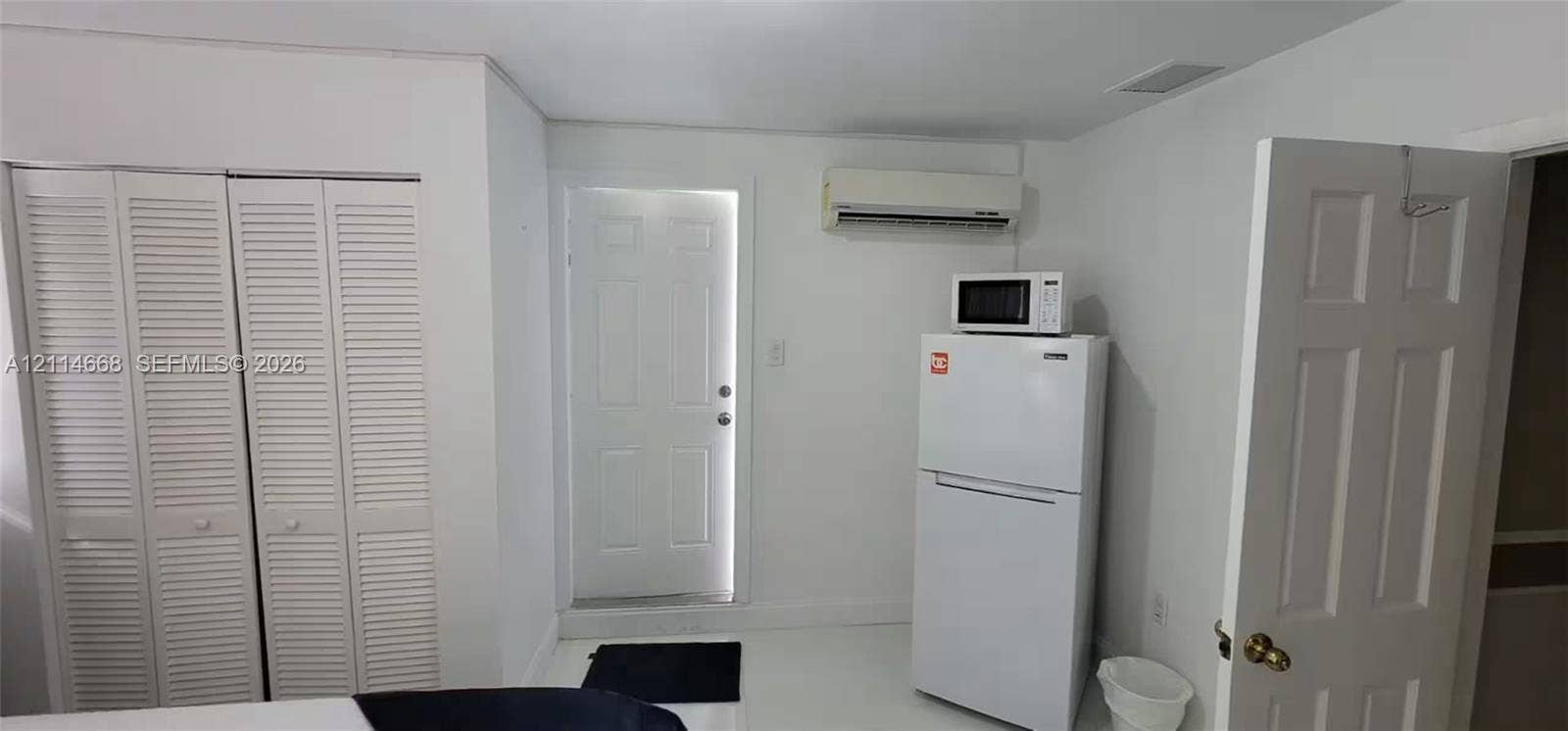 35 SW 28th Road, #B, Miami, Miami, FL 33129 Double louvered-door closet, wall-mounted ductless air conditioning unit, solid-core six-panel door, and white appliance suite featuring a top-freezer refrigerator with microwave