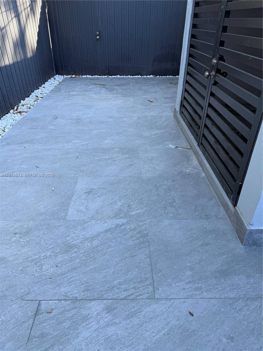 423 NW 32nd Place, Miami, Miami, FL 33125 Outdoor patio featuring large-format stone pavers, white river rock border, and a black metal privacy fence with integrated louvered door