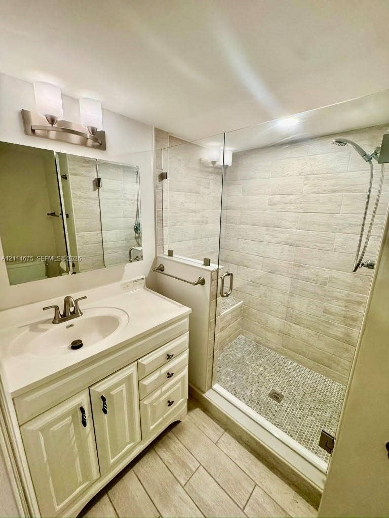 Bathroom featuring a vanity with integrated sink, glass-enclosed shower with tiled walls and pebble-stone flooring, and a mirrored medicine cabinet