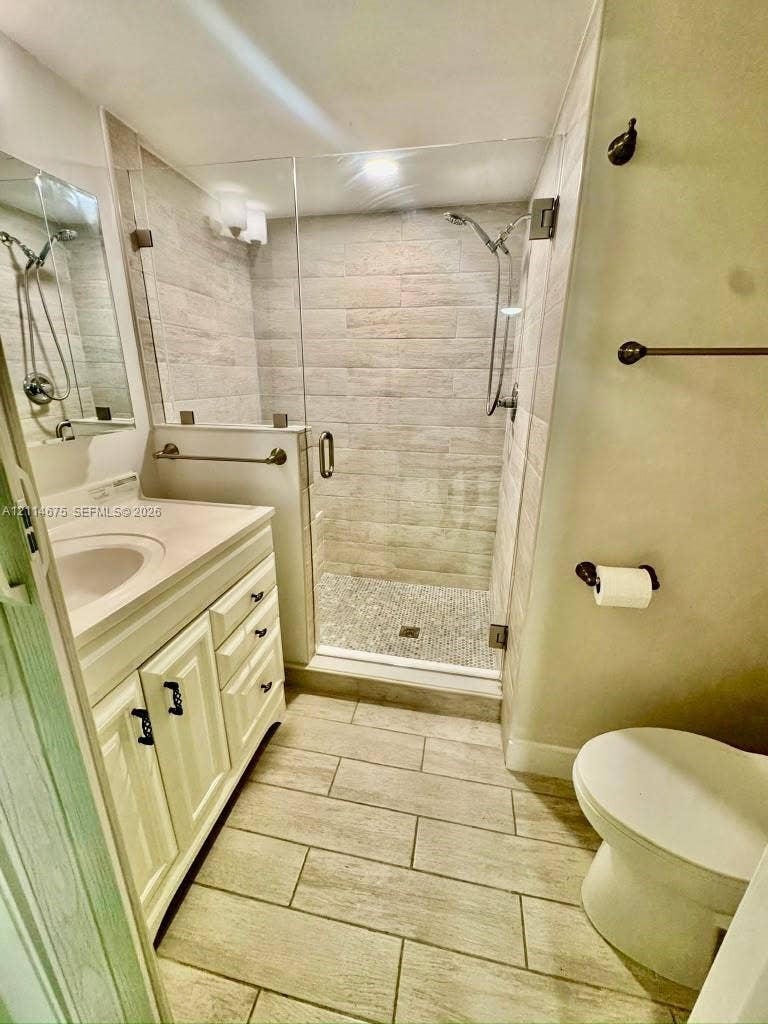 Bathroom featuring a wood-finish tile floor, white cabinetry with a built-in countertop sink, a walk-in shower with stone-tile flooring and glass enclosure, and oil-rubbed bronze fixtures