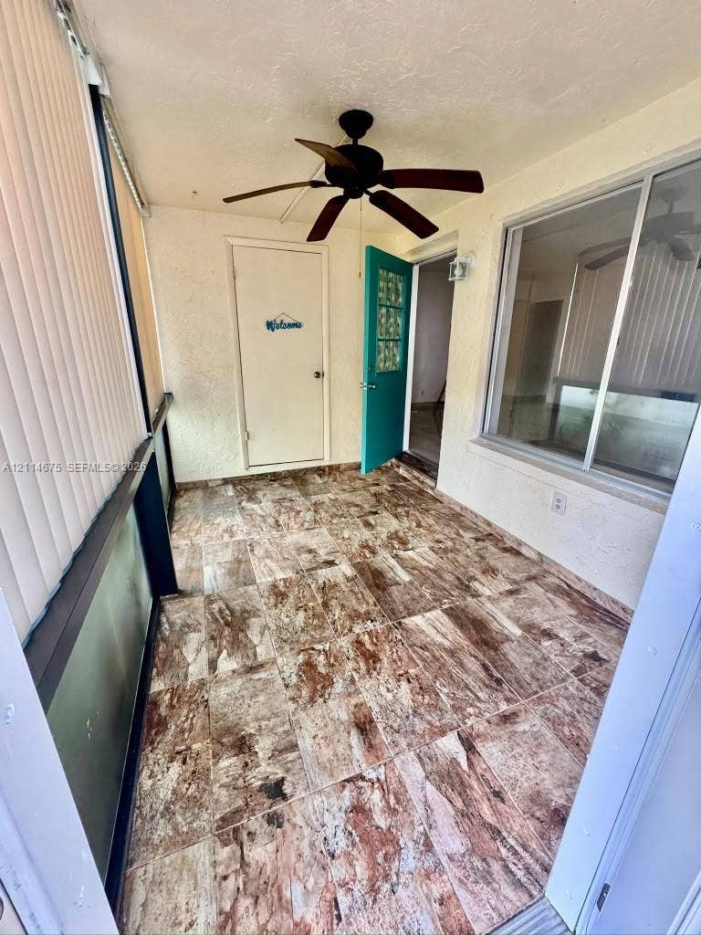 Enclosed porch featuring large-format stone-patterned tile flooring, ceiling fan, and sliding glass window enclosures