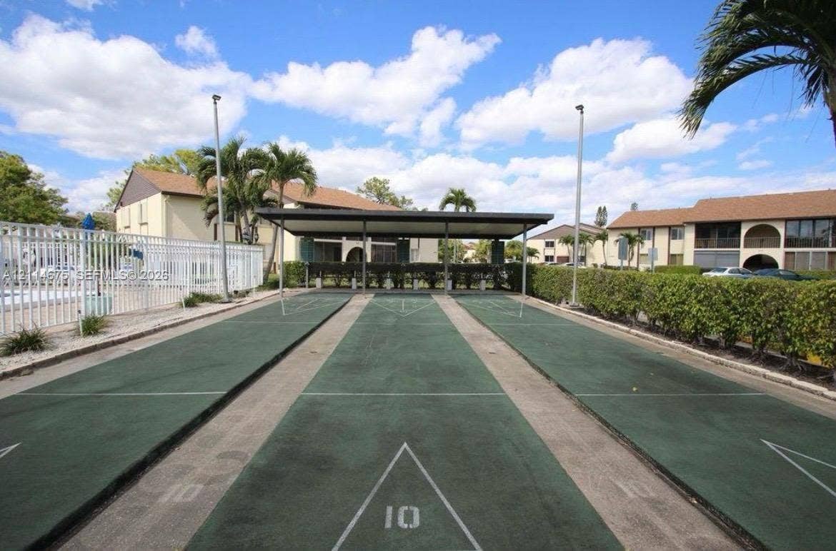 Outdoor shuffleboard court featuring a covered canopy, painted playing surfaces, and perimeter landscaping