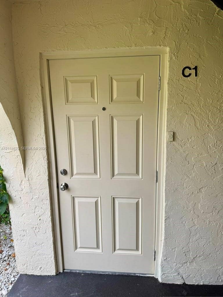 Six-panel entry door featuring a metal knob set, integrated door viewer, and textured exterior wall finish