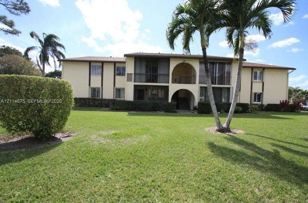 Two-story multi-unit exterior featuring arched architectural detailing, screened-in balcony enclosures, low-slope rooflines, and manicured landscaping