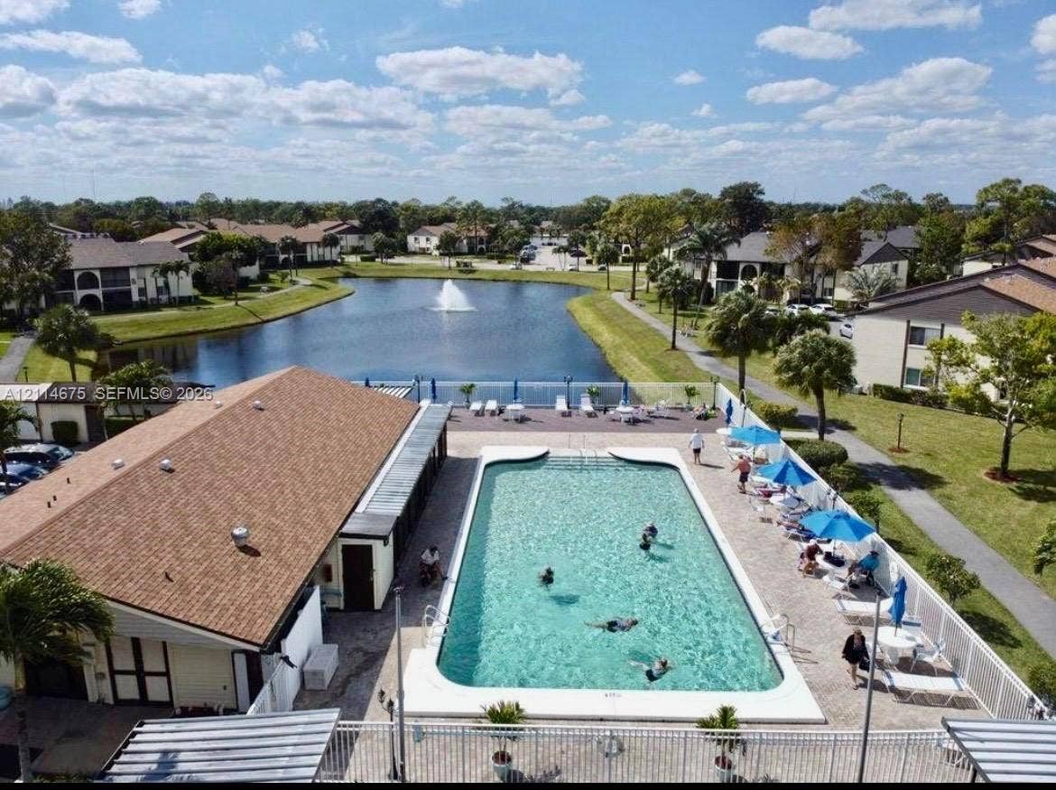 Community swimming pool with concrete decking, clubhouse building, and decorative pond with fountain