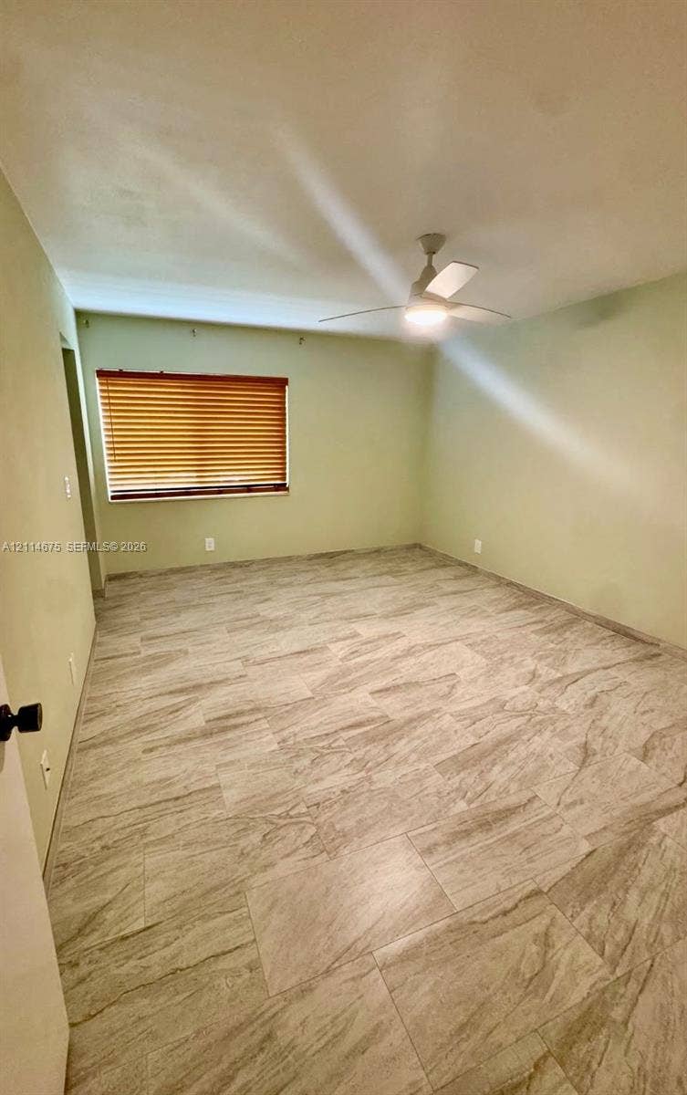 Neutral-toned interior space featuring light-colored tile flooring, a mounted ceiling fan with integrated lighting, and horizontal window blinds
