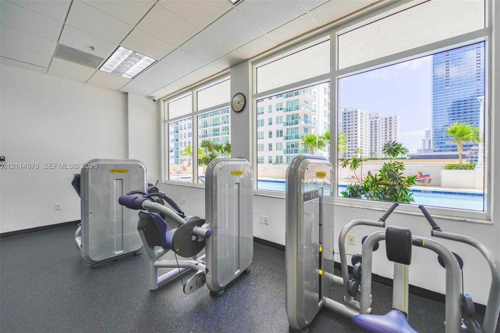 Fitness center featuring rubber flooring, drop ceiling with recessed lighting, and expansive floor-to-ceiling windows providing outdoor scenery