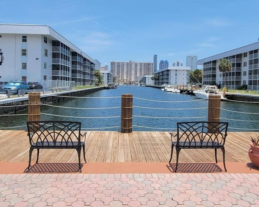 Waterfront bulkhead with a wooden deck, rope railings, and patterned stone paver patio