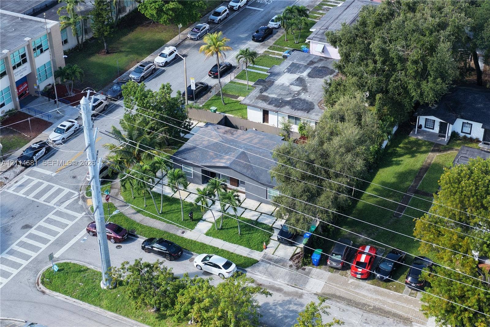 6700 NW 5th Avenue, Miami, FL 33150 Single-story residence featuring a dark-toned exterior, concrete paver driveway with grass infill, and established landscaping including mature trees and palms