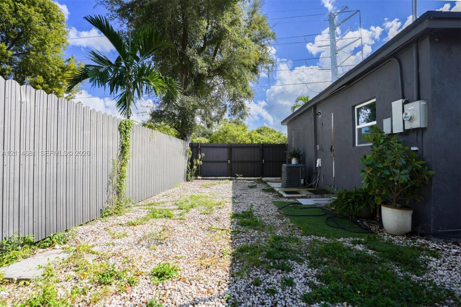 6700 NW 5th Avenue, Miami, FL 33150 Side yard enclosed by corrugated metal fencing, featuring a gravel surface, palm tree, and gated entry