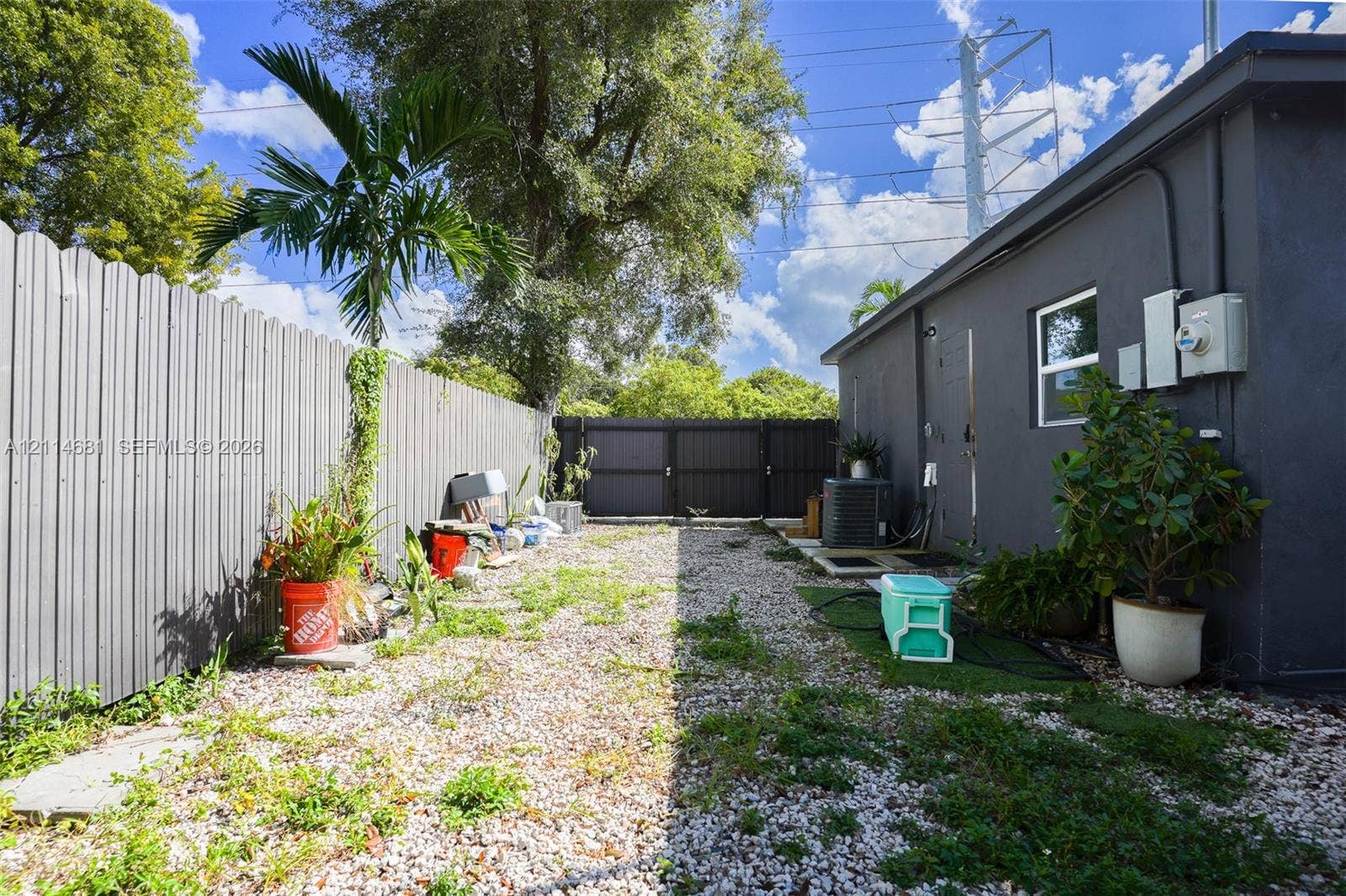 6700 NW 5th Avenue, Miami, FL 33150 Exterior side yard featuring gravel ground cover, a vertical corrugated metal fence, and a gated perimeter enclosure