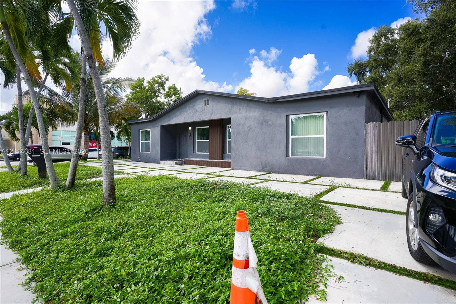 6700 NW 5th Avenue, Miami, FL 33150 Single-story exterior featuring a dark-toned stucco facade, a grid-pattern concrete paver driveway, and a covered front entry with wood-texture paneling