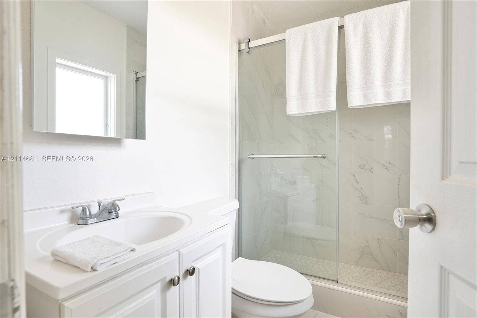 6700 NW 5th Avenue, Miami, FL 33150 Bathroom featuring a white vanity with an integrated sink, polished chrome dual-handle faucet, wall-mounted mirror, and a shower enclosure with glass sliding doors and stone-patterned wall tile