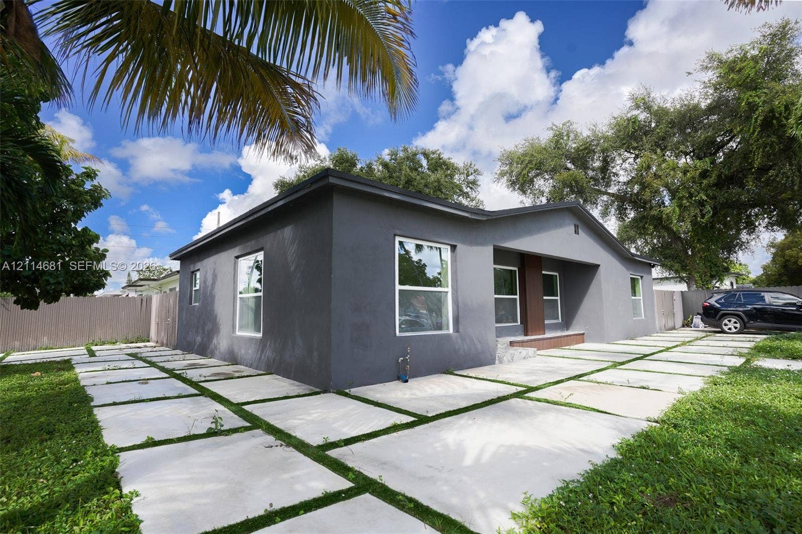6700 NW 5th Avenue, Miami, FL 33150 Single-story exterior featuring a dark-toned stucco facade, grid-patterned concrete paver driveway, and a recessed entryway with a wooden accent pillar