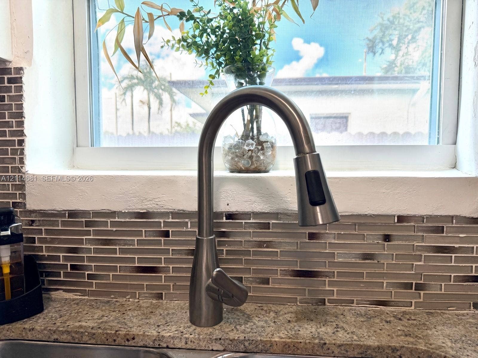 6700 NW 5th Avenue, Miami, FL 33150 High-arc pull-down faucet with a brushed metallic finish, set against a multi-toned glass tile backsplash and stone countertop with an integrated basin
