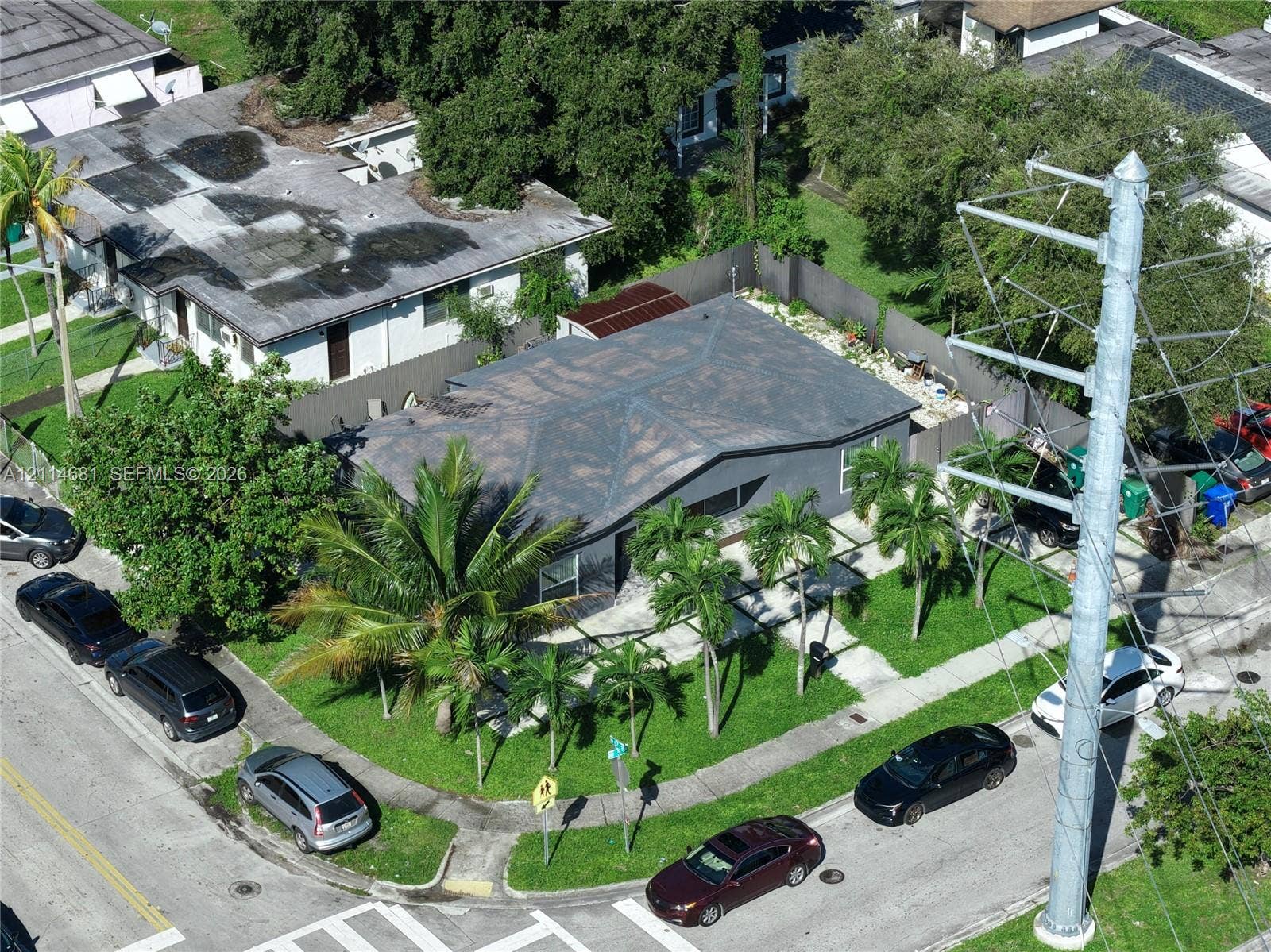 6700 NW 5th Avenue, Miami, FL 33150 Corner lot property featuring a low-slope roof, mature palm trees, and an enclosed rear yard area