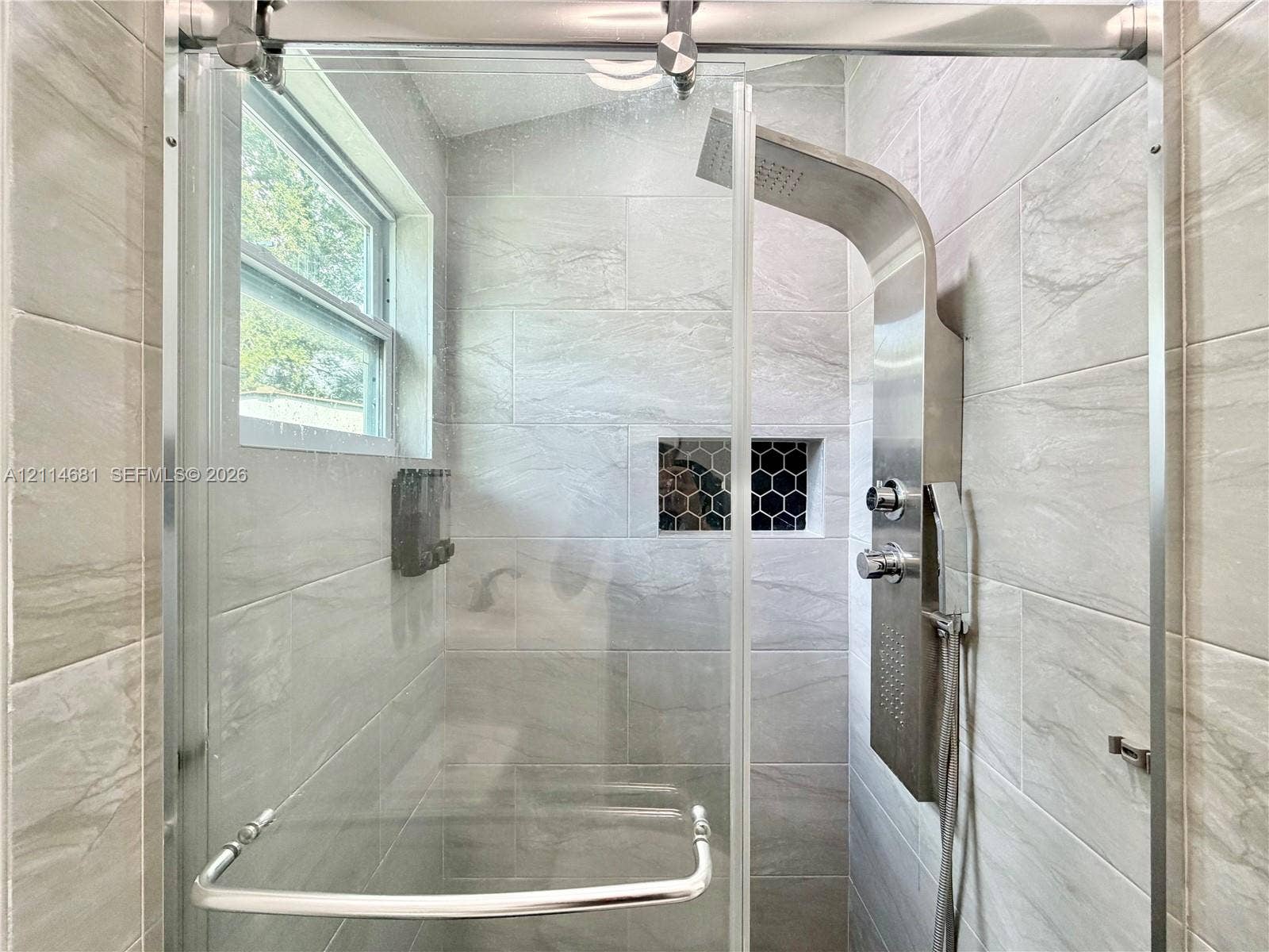 6700 NW 5th Avenue, Miami, FL 33150 Walk-in shower featuring large-format porcelain tile, a stainless steel rainfall shower panel, a sliding glass door system, and a built-in recessed niche with decorative hexagon tile inlay