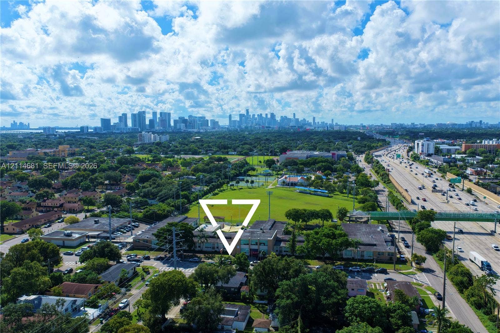 6700 NW 5th Avenue, Miami, FL 33150 Aerial perspective of the property grounds featuring a multi-story building, established mature trees, proximity to expansive green space, and a backdrop of the urban skyline