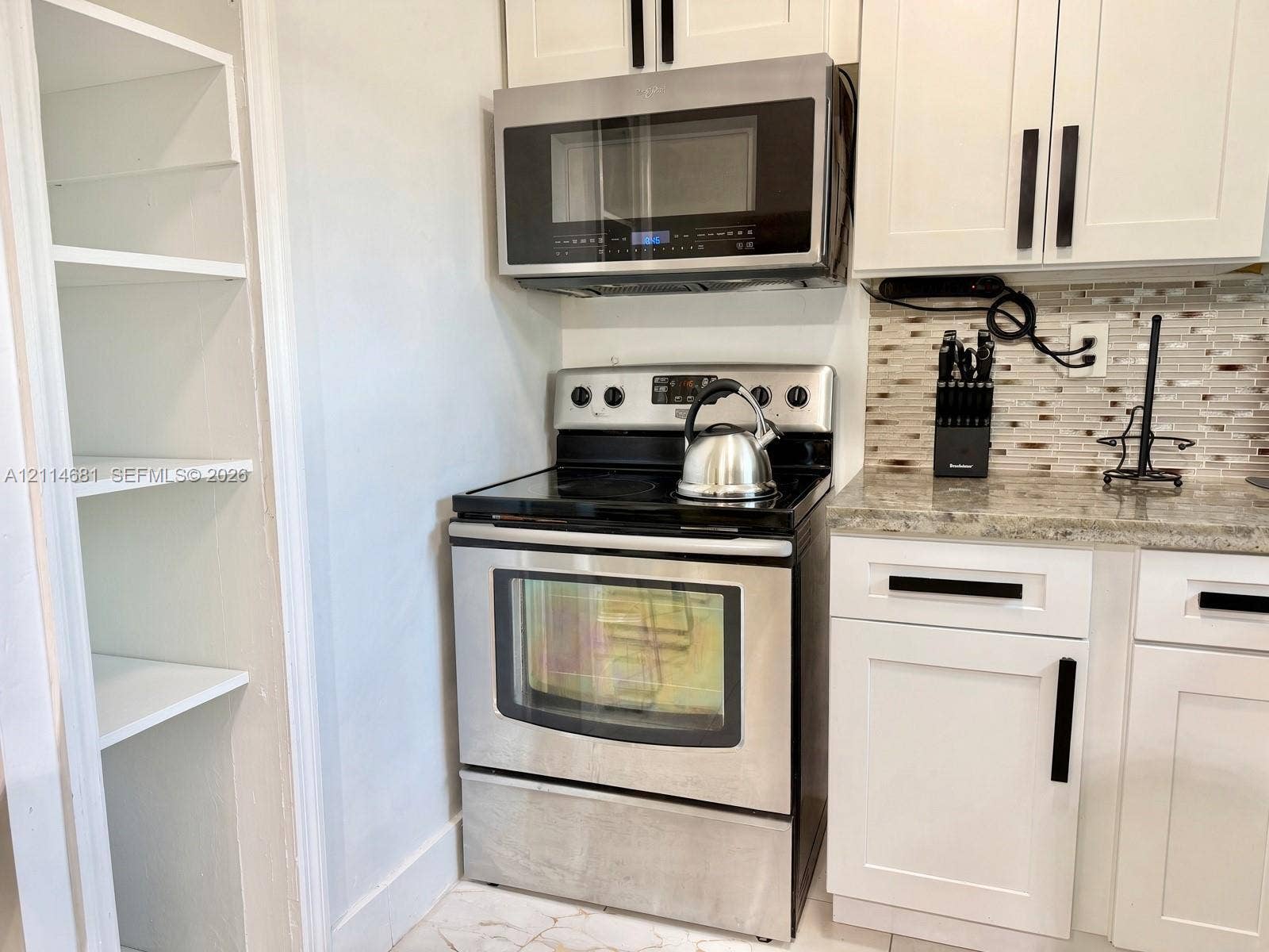 6700 NW 5th Avenue, Miami, FL 33150 Kitchen featuring white shaker-style cabinetry with matte black hardware, stainless steel appliances, a multi-tonal tile backsplash, stone-finish countertops, and an integrated open shelving pantry