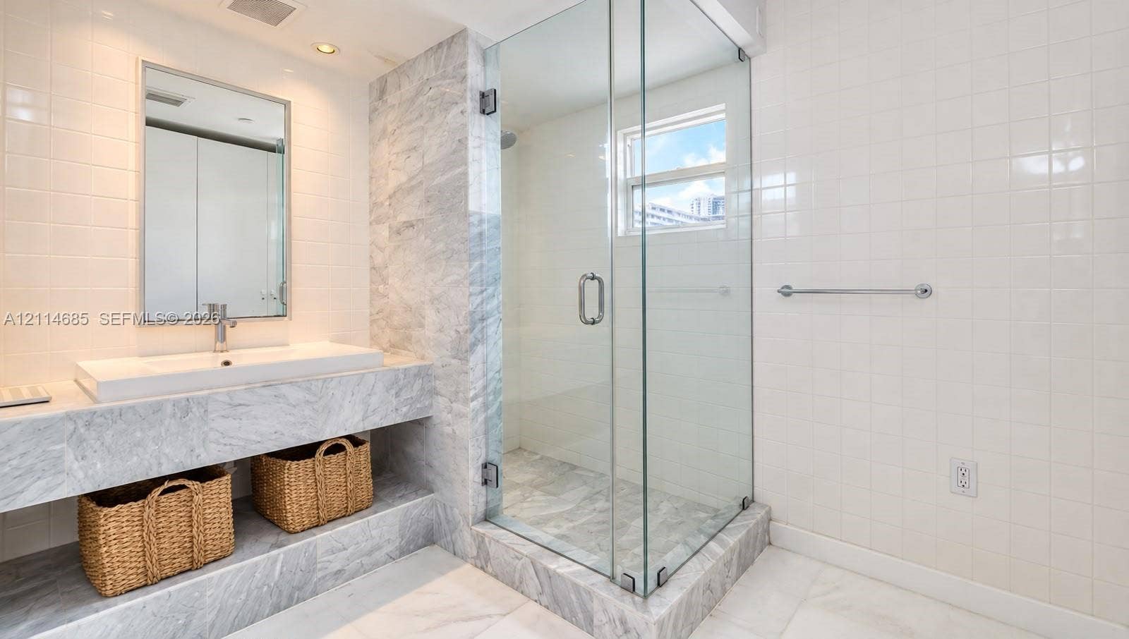 1035 West Avenue, #704, Miami Beach, FL 33139 Stone-surfaced vanity featuring a rectangular integrated sink, glass-enclosed shower, polished stone tiling, and wall-mounted metal towel bar