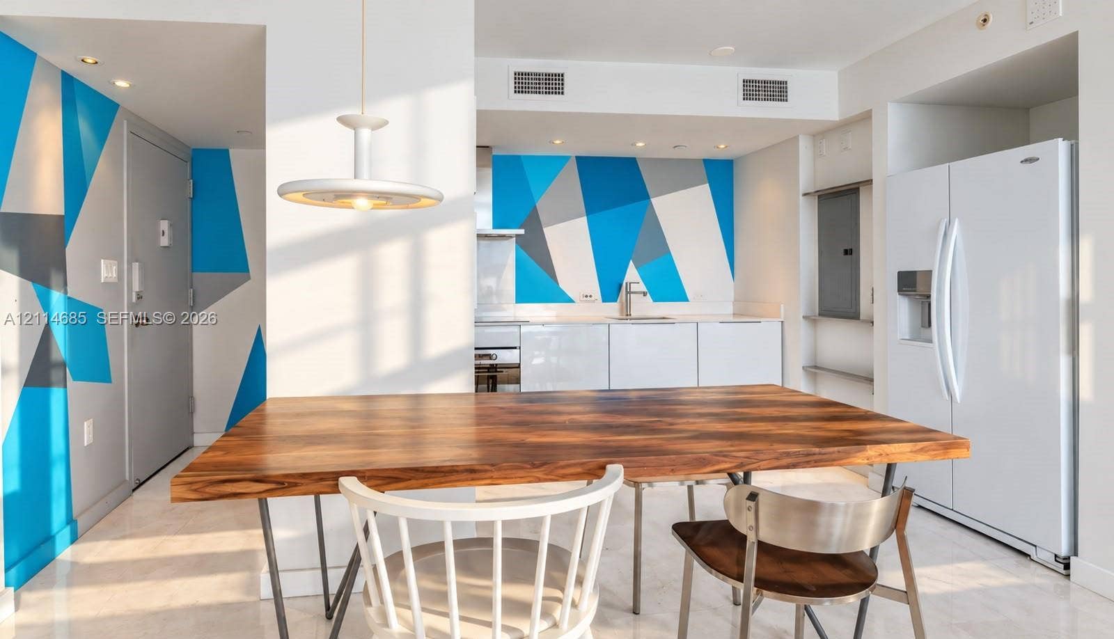 1035 West Avenue, #704, Miami Beach, FL 33139 Kitchen featuring minimalist white cabinetry, a full-size refrigerator, a geometric wall mural, and a pendant light fixture