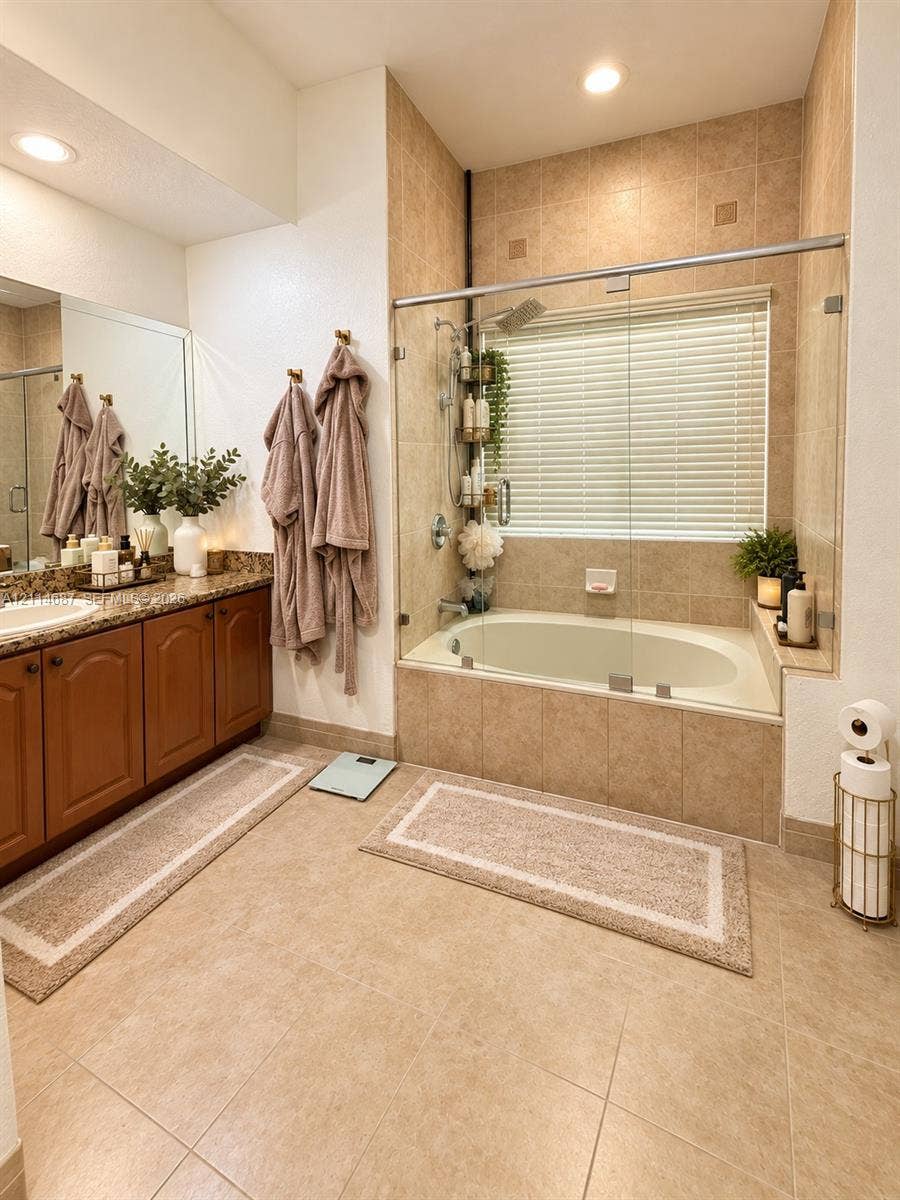 Bathroom featuring a tiled surround soaking tub, frameless glass shower enclosure, wood cabinetry, stone-finish countertop with an integrated sink, and recessed lighting