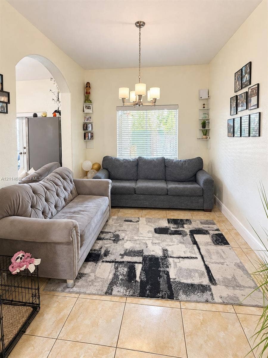 Ceramic tile flooring, arched entryway, four-light brushed-nickel chandelier, and wall-mounted shelving units