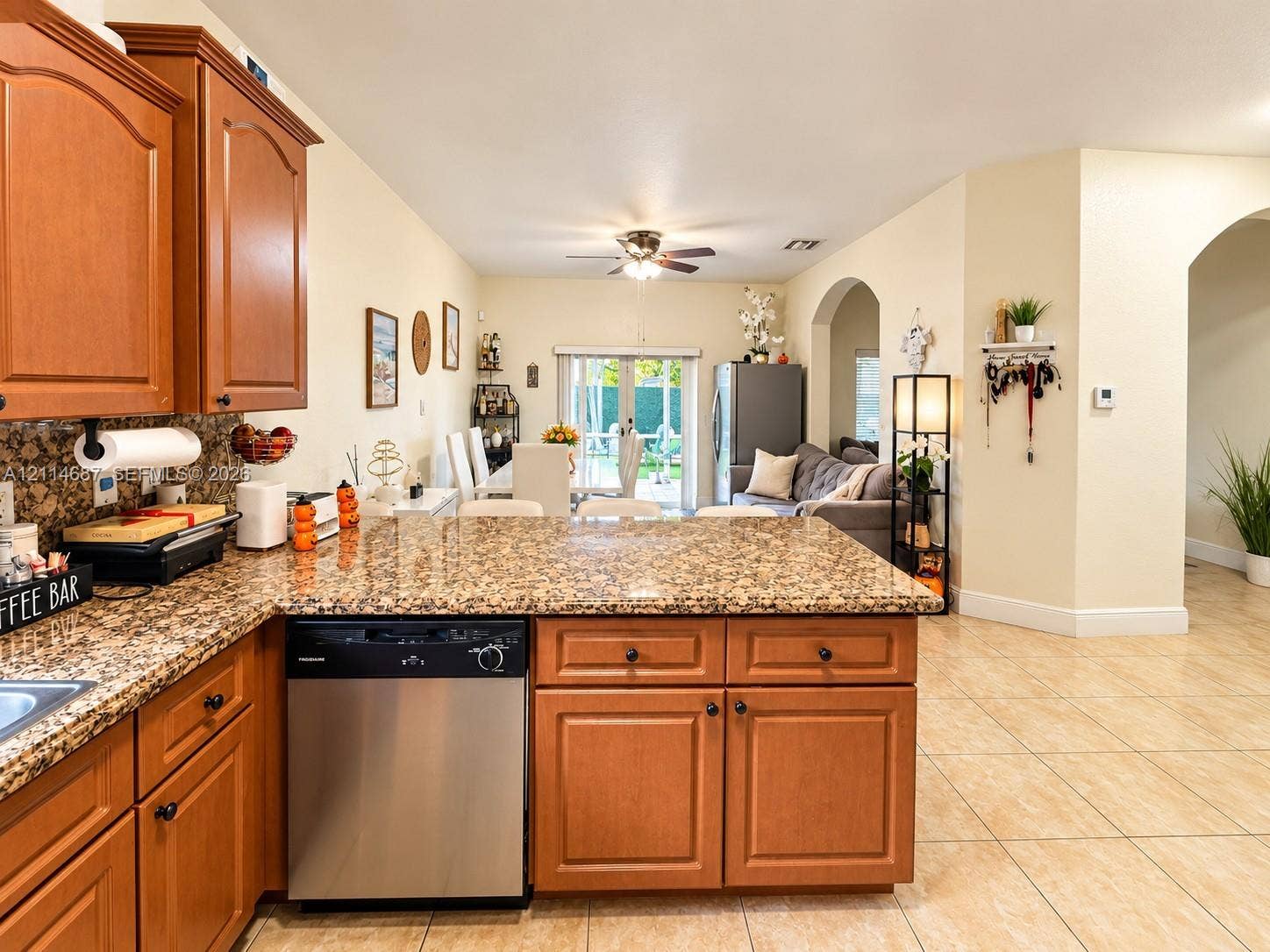 Kitchen featuring wood cabinetry, stone-surface countertops, stainless steel dishwasher, tile flooring, and arched interior entryways