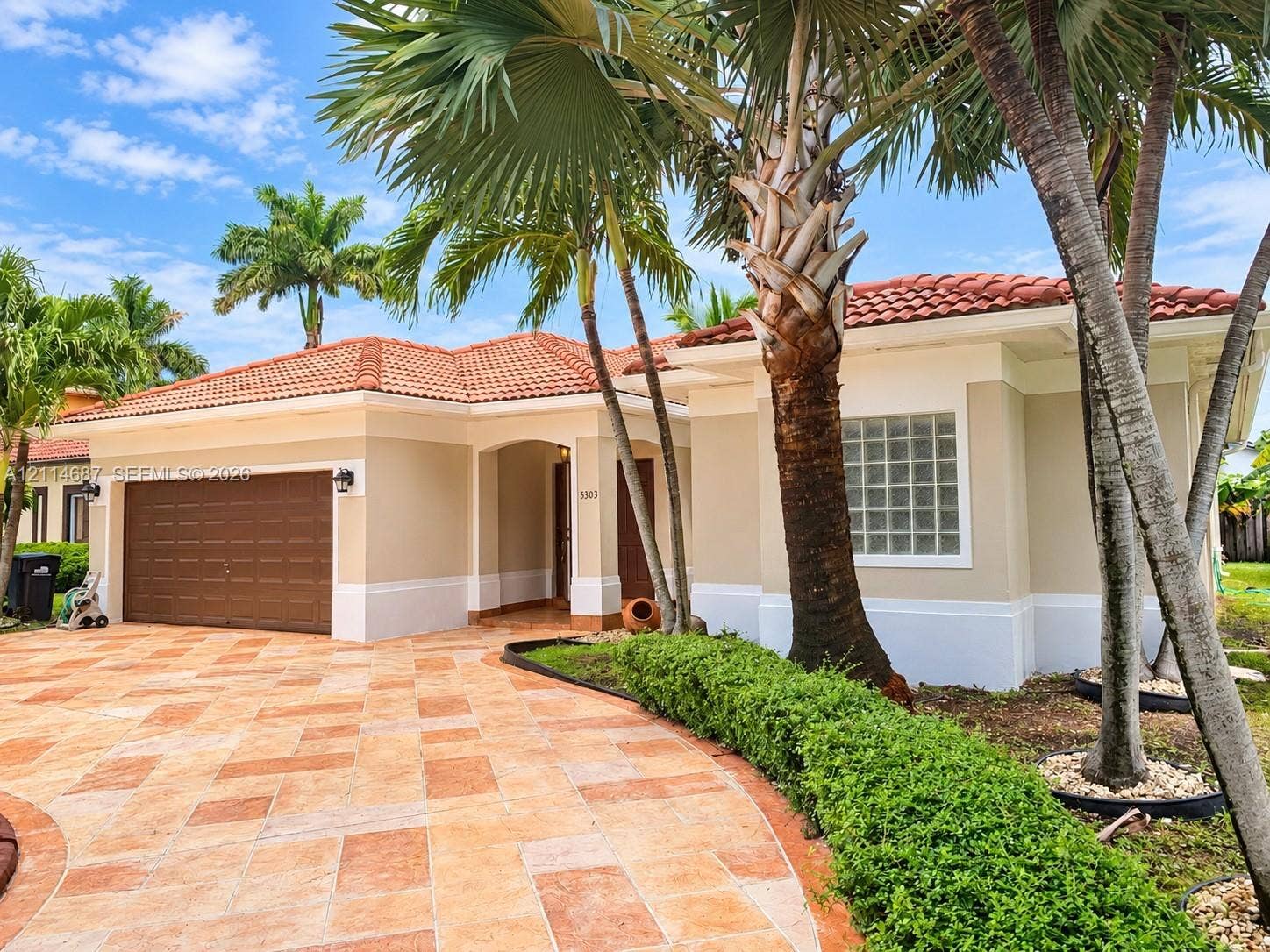 Exterior featuring a tile roof, stucco finish, paver driveway, glass block window, and mature palm trees