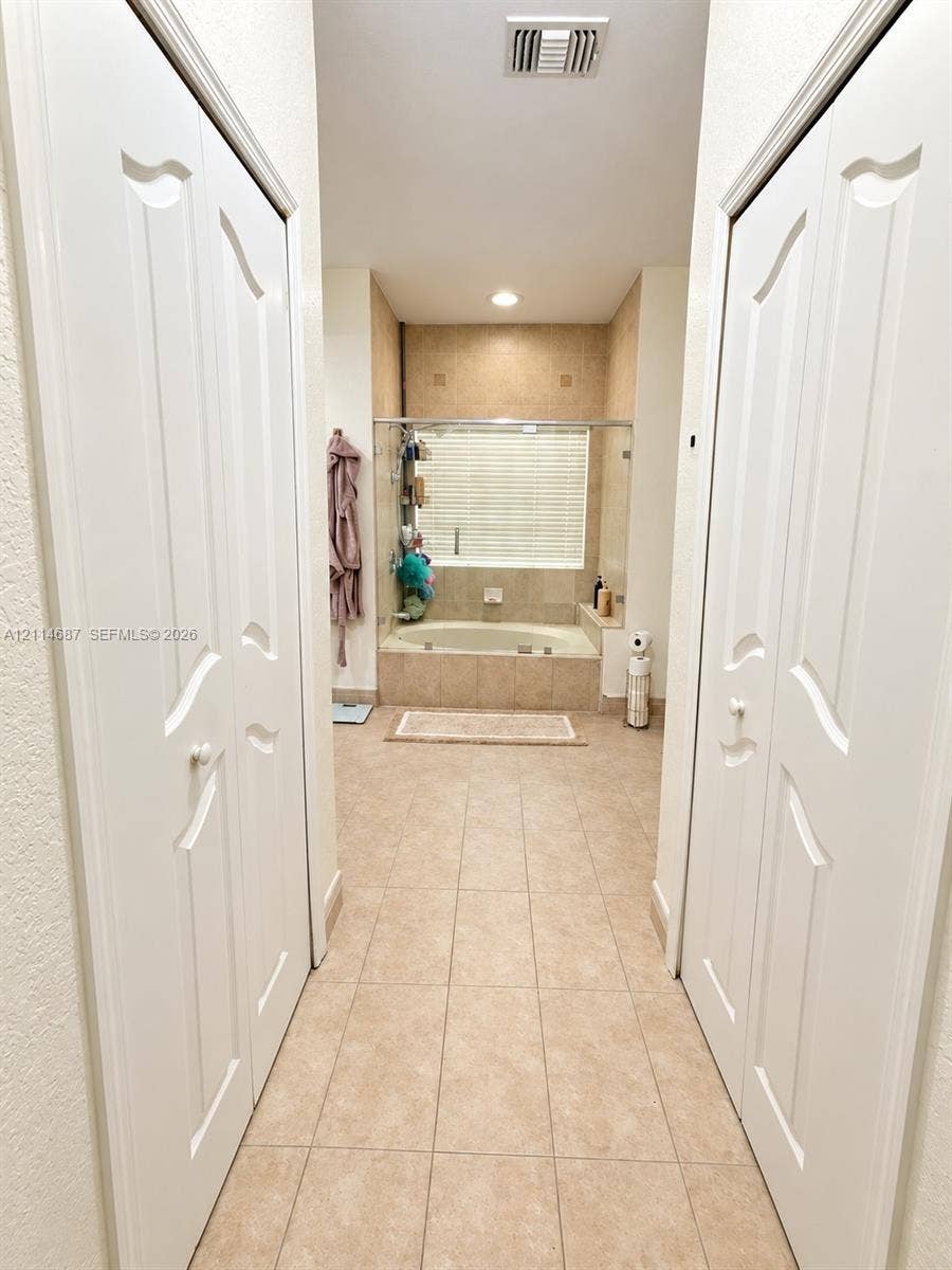 Built-in dual-panel closet doors, recessed lighting, and tile flooring, featuring a tiled soaking tub with glass enclosure