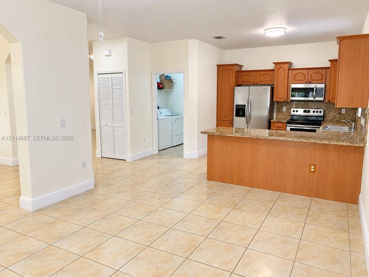 Kitchen featuring wood cabinetry, stone-finish countertops, stainless steel appliances, a breakfast bar, and tile flooring