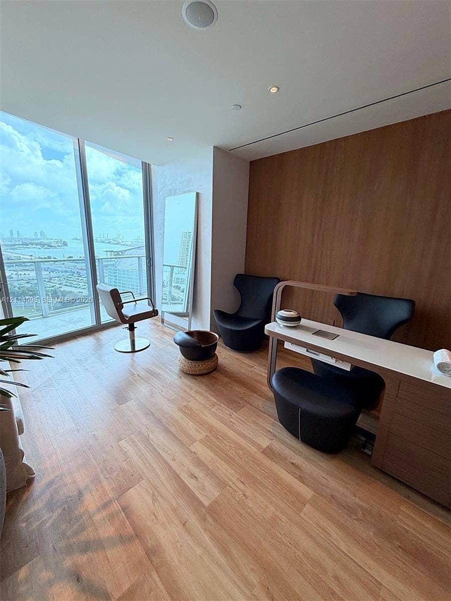 Floor-to-ceiling windows, wood-finish flooring, full-height wood-panel accent wall, recessed ceiling lighting, and glass-railing exterior balcony