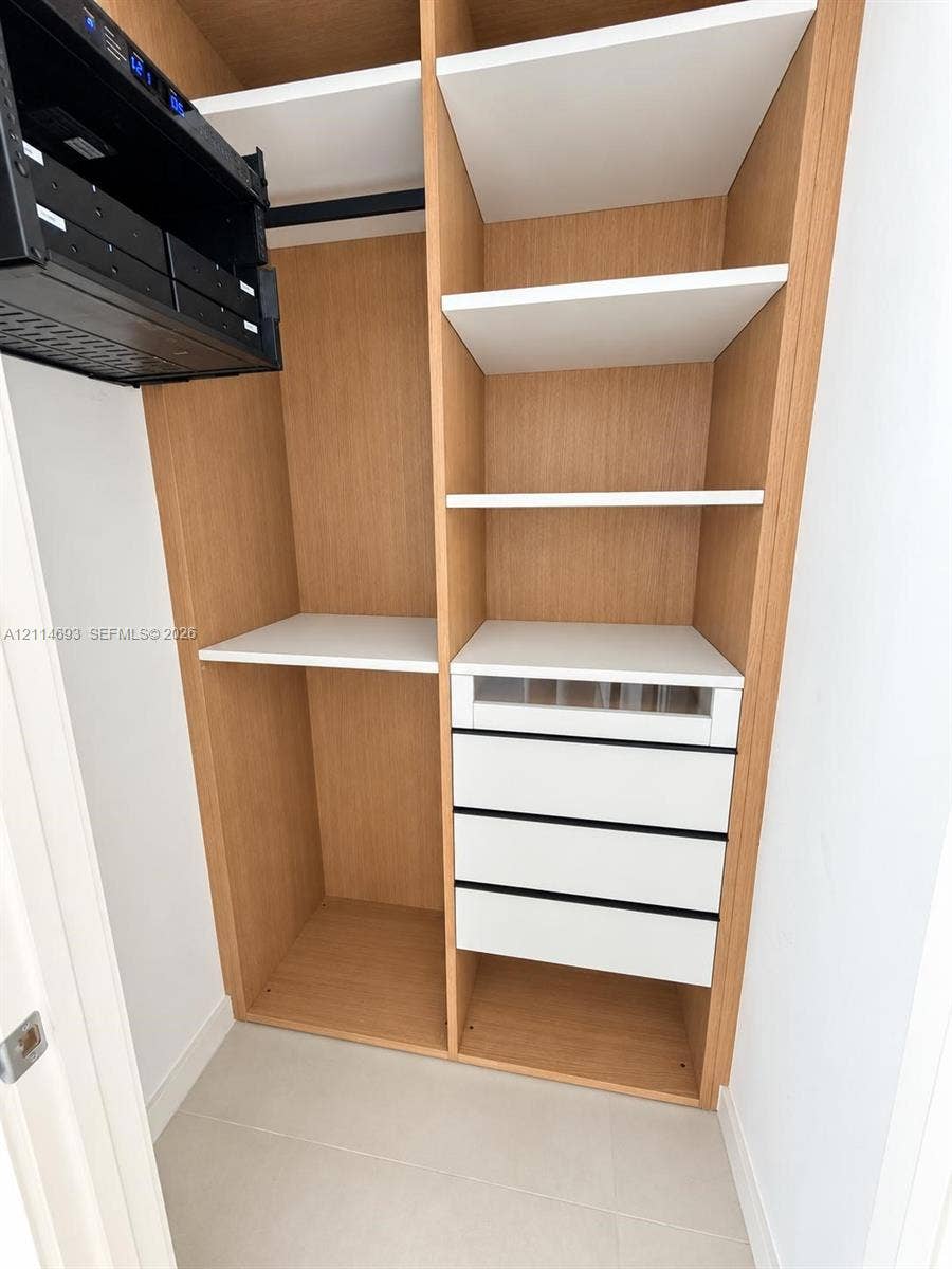 Built-in closet system featuring natural wood-finish cabinetry, adjustable white shelving, a glass-front accessory drawer, and three soft-close storage drawers