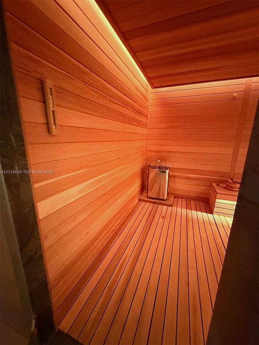 Sauna featuring wood-plank walls, integrated linear ceiling lighting, slatted wood flooring, a stainless steel heater, and built-in wood bench seating