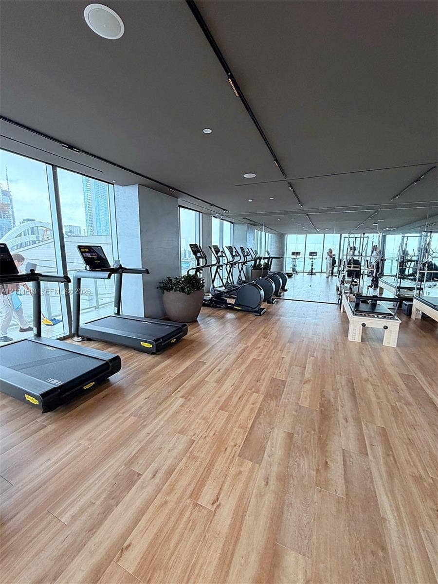 Fitness center featuring wood-finish flooring, floor-to-ceiling windows, integrated track lighting, and mirrored wall surfaces