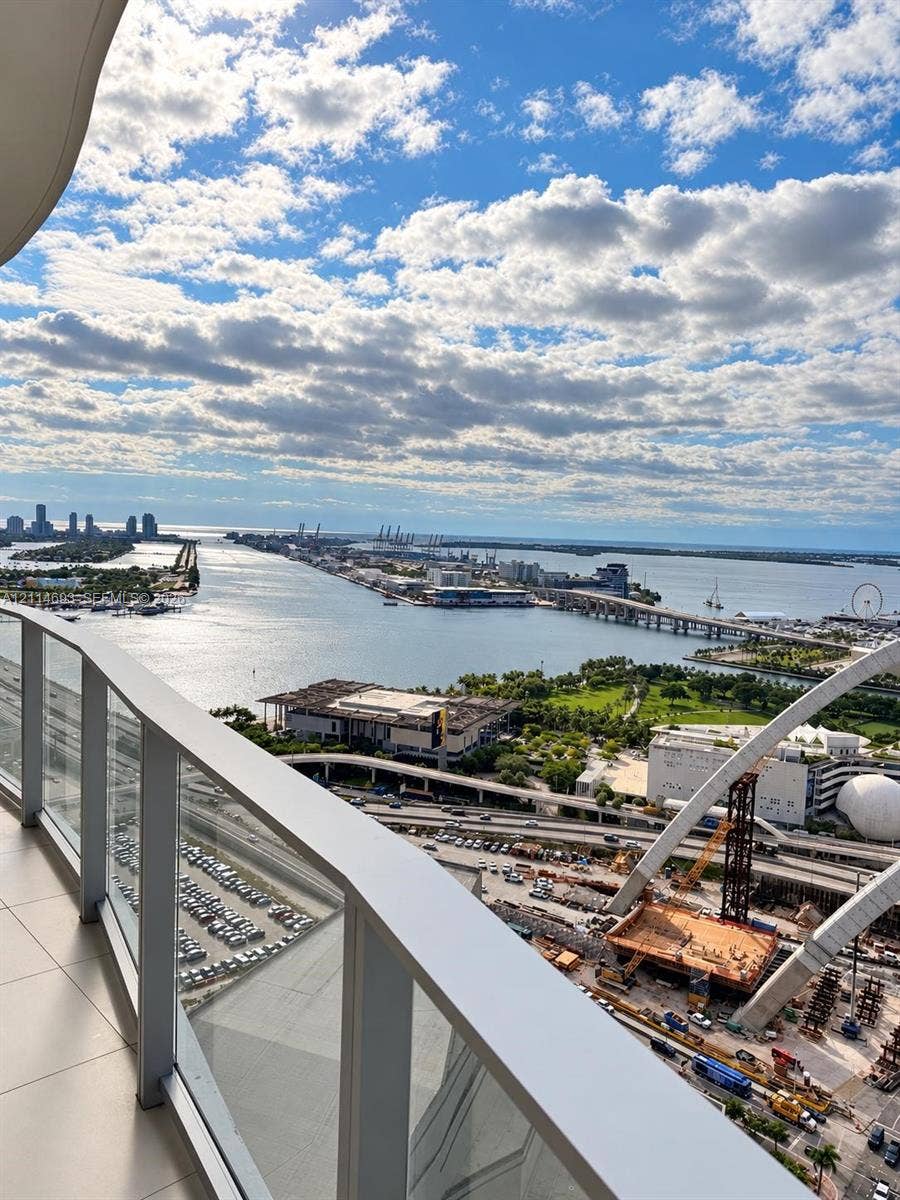 Private balcony featuring glass panel railing and tile flooring, offering a wide-angle perspective of the harbor, bridges, and surrounding cityscape
