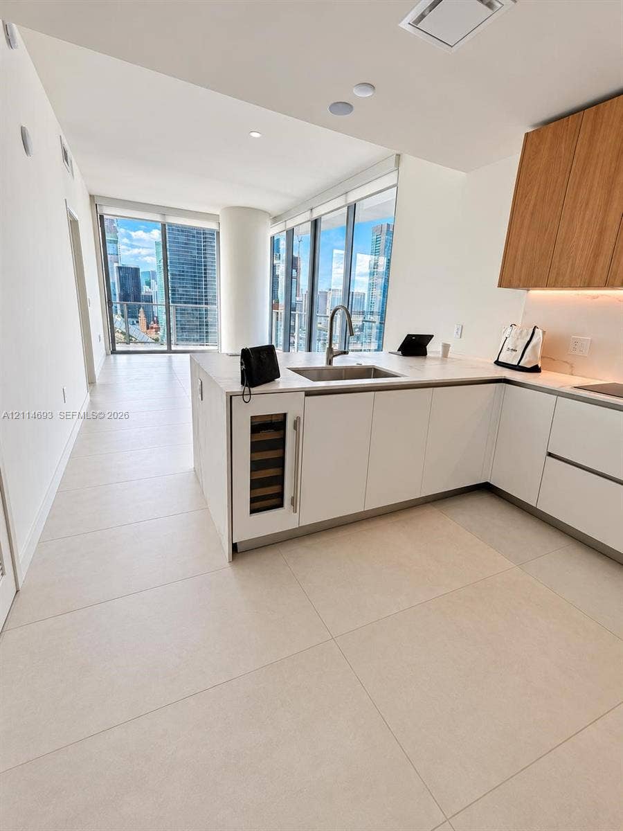Kitchen featuring white flat-panel cabinetry, wood-finish upper cabinets, solid-surface countertops, an integrated wine refrigerator, and floor-to-ceiling windows