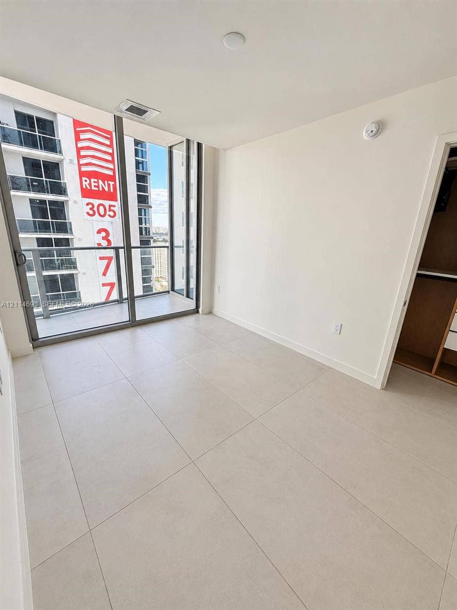 Floor-to-ceiling glass windows, neutral tile flooring, glass-railed private balcony, and built-in closet shelving