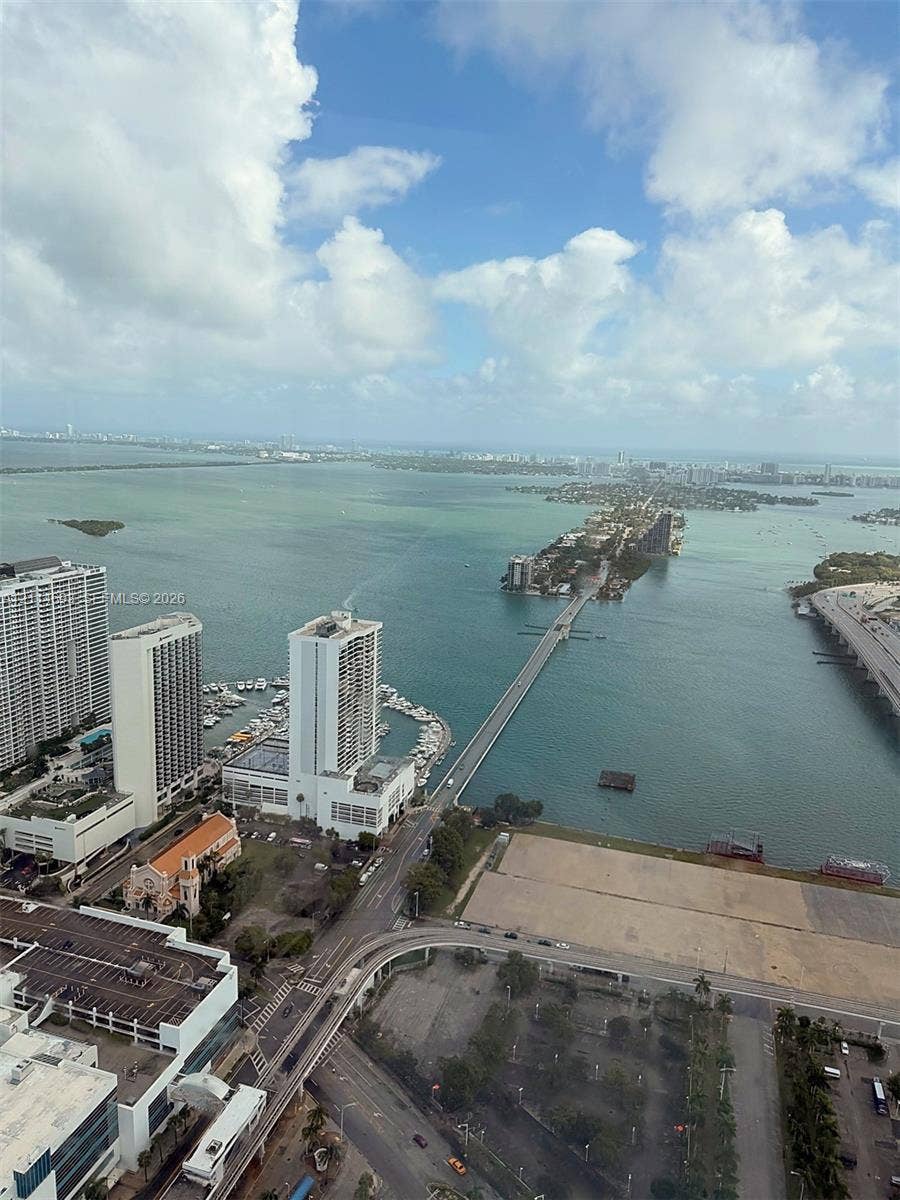 Elevated perspective featuring coastal water scenery, a bridge crossing, metropolitan high-rise architecture, and marina access