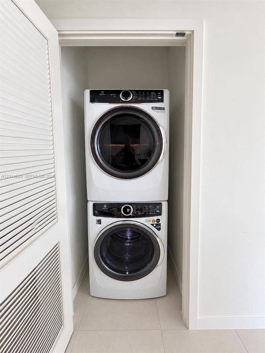Stacked front-load laundry pair with a white finish, enclosed in a closet featuring a louvered door