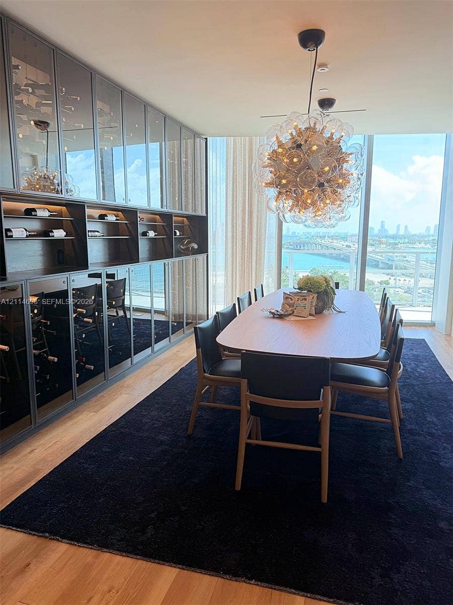 Floor-to-ceiling custom wine storage with glass-front cabinetry and integrated LED accent lighting, light-toned wood-finish flooring, and a decorative multi-bulb statement chandelier