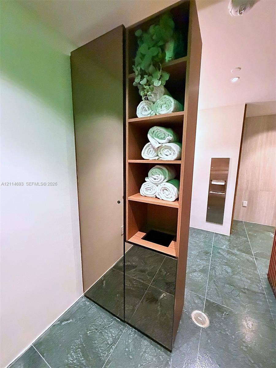 Full-height built-in cabinetry featuring open shelving and a solid-panel door, set against stone-finish floor tiling with a stainless steel wall-mounted dispenser