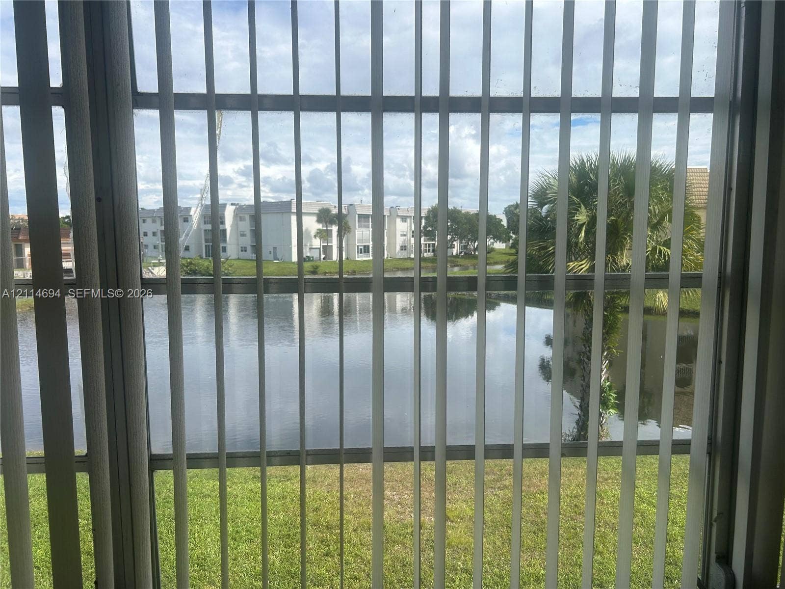 8600 Sunrise Lakes Boulevard, #211, Sunrise, Sunrise, FL 33322 Vertical blind window treatment overlooking a pond, manicured lawn, and mature palm tree
