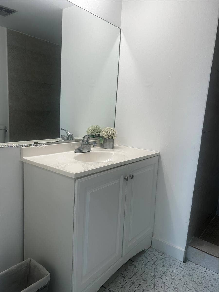 8600 Sunrise Lakes Boulevard, #211, Sunrise, Sunrise, FL 33322 Bathroom vanity featuring white shaker-style cabinetry, an integrated basin, a polished chrome faucet, and a large wall-mounted mirror over geometric-patterned tile flooring