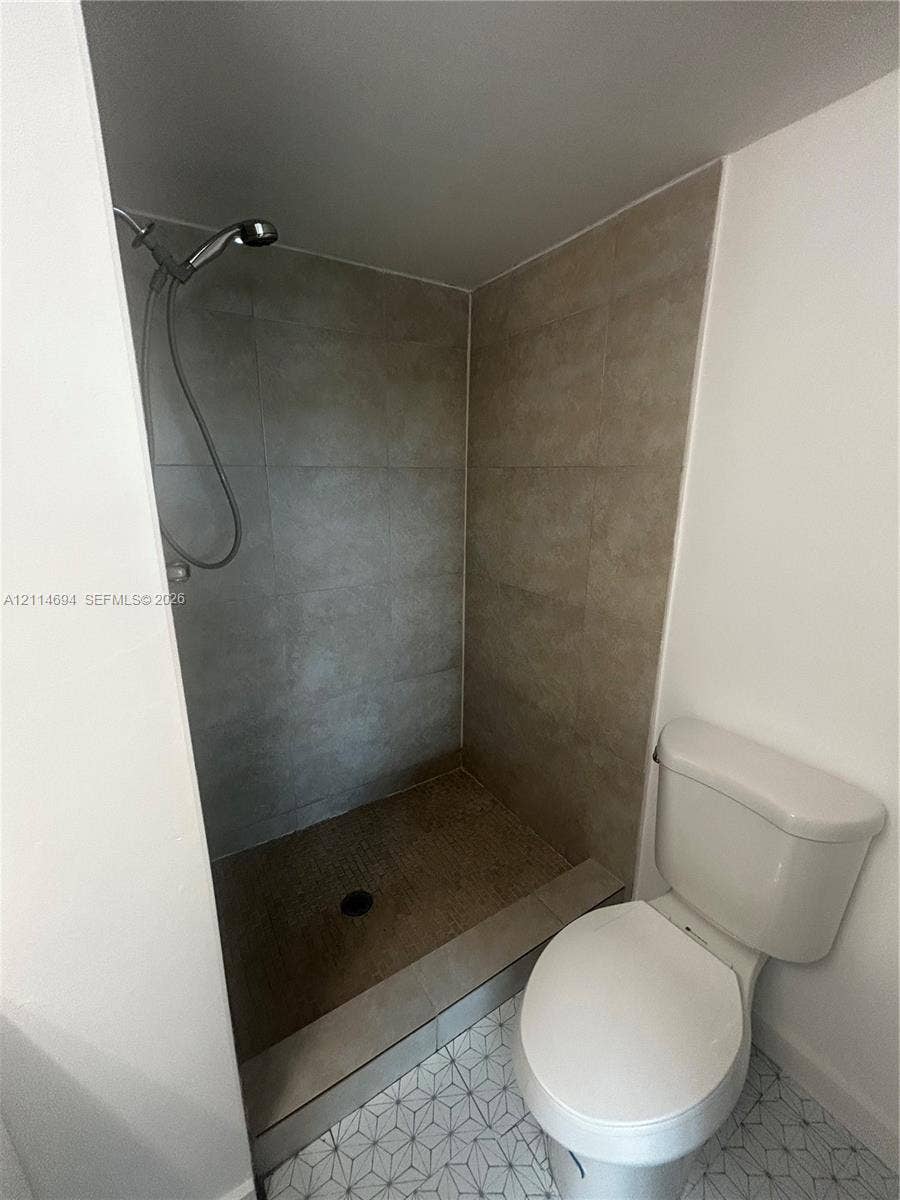 8600 Sunrise Lakes Boulevard, #211, Sunrise, Sunrise, FL 33322 Shower stall featuring large-format neutral-toned tile walls and a handheld shower head, complemented by a floor with geometric patterned tile and a standard-profile toilet
