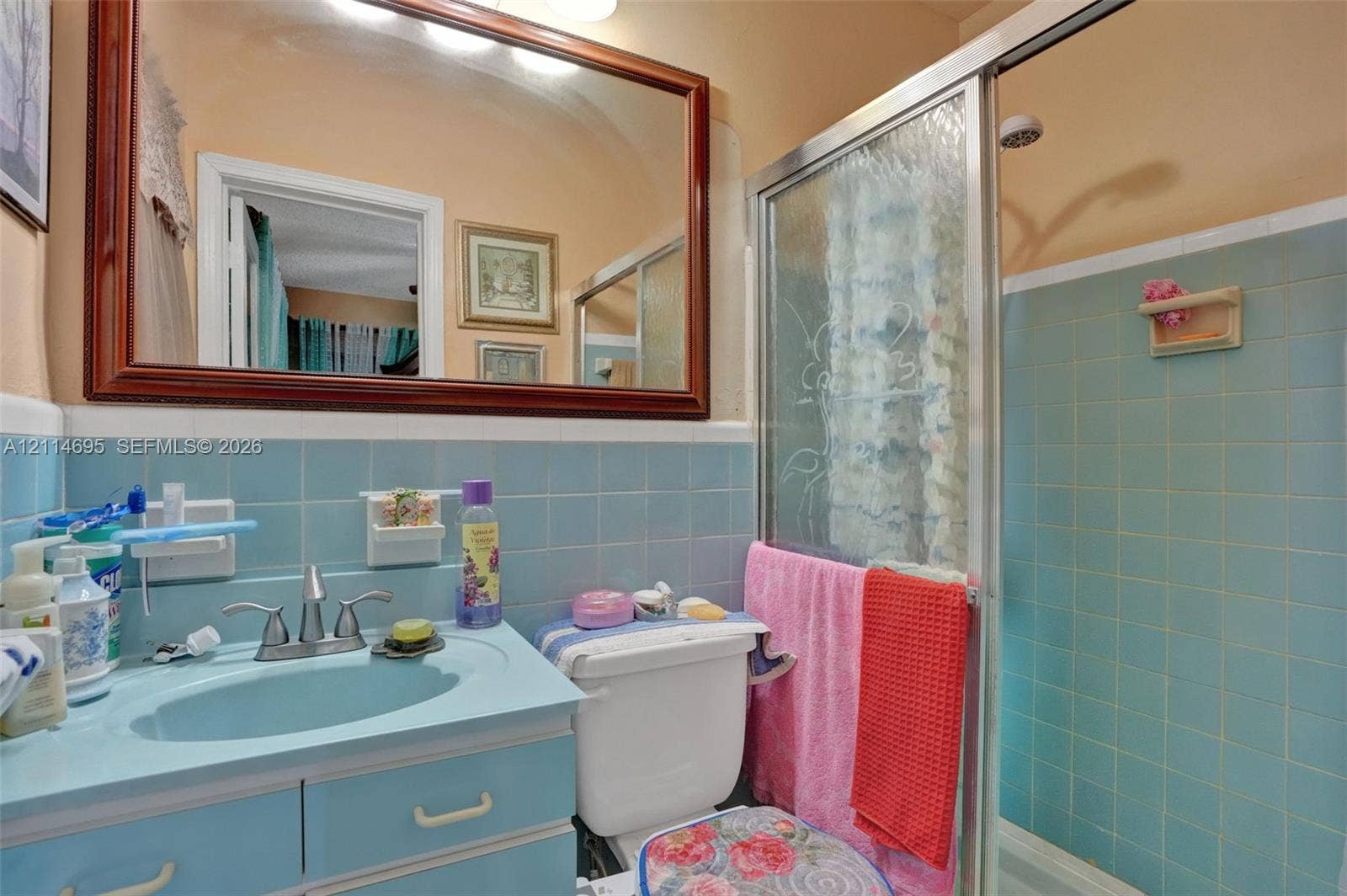 Bathroom featuring a vanity with an integrated basin, a large wood-framed mirror, and blue tiled wall accents surrounding the shower enclosure with a sliding glass door