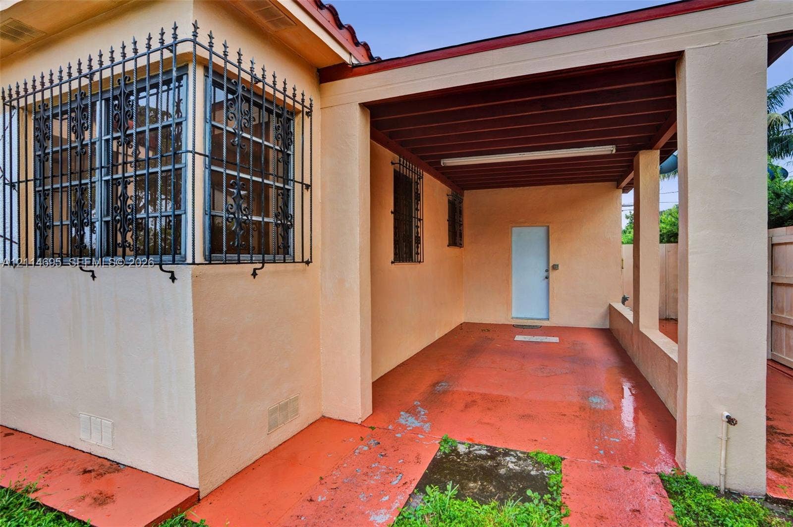 Covered exterior patio featuring a concrete floor, decorative metal window security bars, a flat-roof overhang, and stucco siding