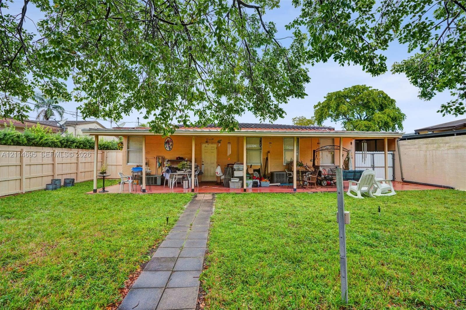 Fenced backyard featuring a concrete pathway, covered patio, and mature trees